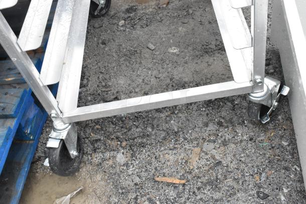 Commercial pan transport rack with sturdy metal frame on commercial casters, shows signs of outdoor use.