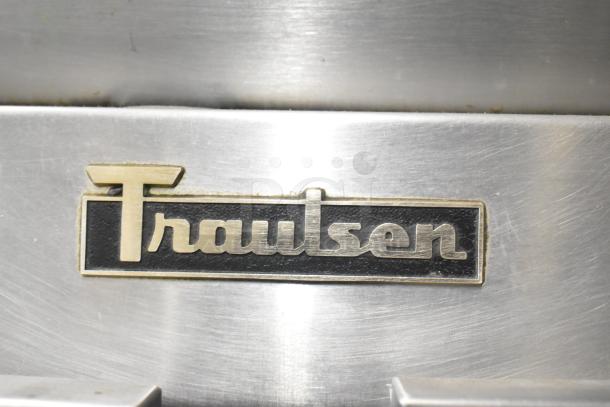 Traulsen logo on stainless steel surface of a commercial 4 half-size door reach-in refrigerator, on casters.