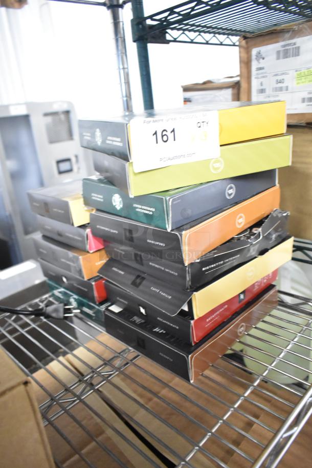 Stack of 14 beverage boxes, including LavAzza Vanilla Latte Mix and Starbucks Coffee/Espresso Roasts, on a metal shelf.