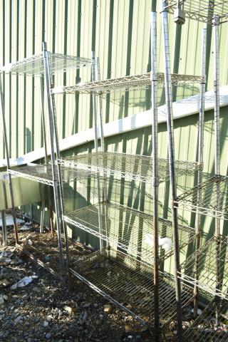 Chrome finish 4-tier wire shelving unit, standing outdoors. Noticeable wear. Buyer must dismantle for shipping.