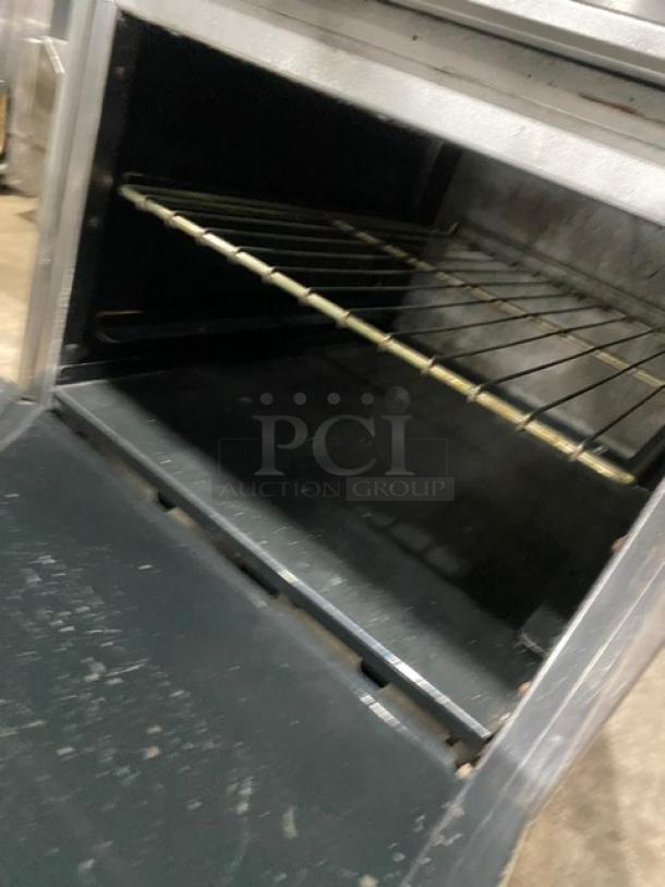 American Range commercial stainless steel 4-burner range/oven combo, includes back splash, overhead salamander shelf, and wired oven rack. Mounted on legs.