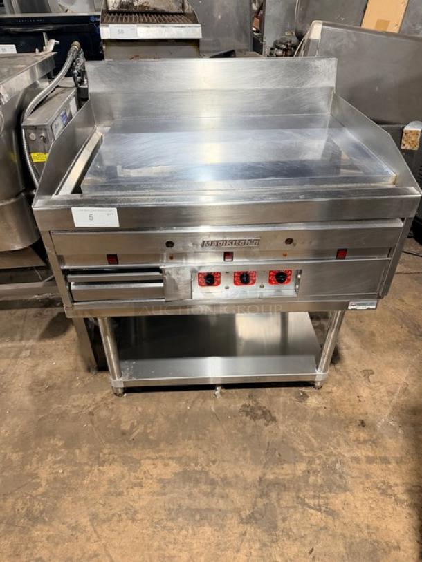 MagiKitch'n natural gas commercial griddle with mirror shine on a stainless steel stand. Thermostatic controls visible.