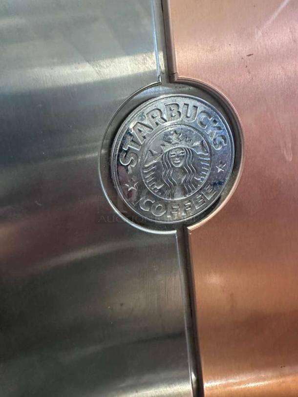 Starbucks Mastrena espresso machine emblem, showcasing brand logo on a metal surface, representing commercial quality.