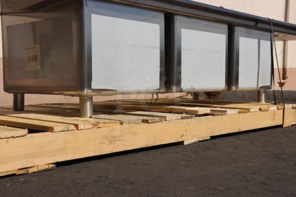 Regency 600S31824224 106" 16 gauge stainless steel three compartment sink with two 24" drainboards on a wooden pallet.