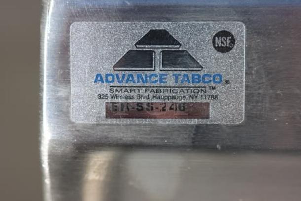 Advance Tabco EK-SS-246 label on stainless steel cabinet base work table, showing brand, model, and NSF certification.
