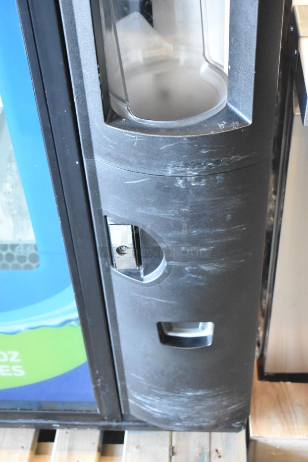 Commercial bottled drink vending machine with bill acceptor, showing moderate wear, black outer panel, on wooden pallet.