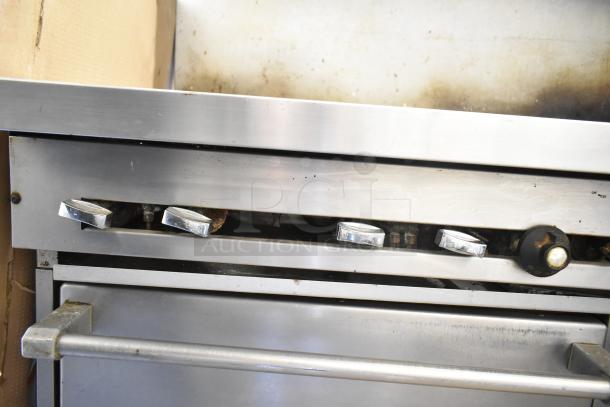 Commercial gas-powered 10 burner range with 2 ovens, overhead shelf, and backsplash. Features chrome knobs and metal build. Used condition.