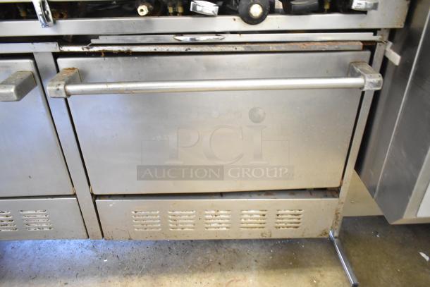 Commercial gas-powered 10 burner range with dual ovens, shelf, and backsplash. Used condition, visible wear and surface rust.