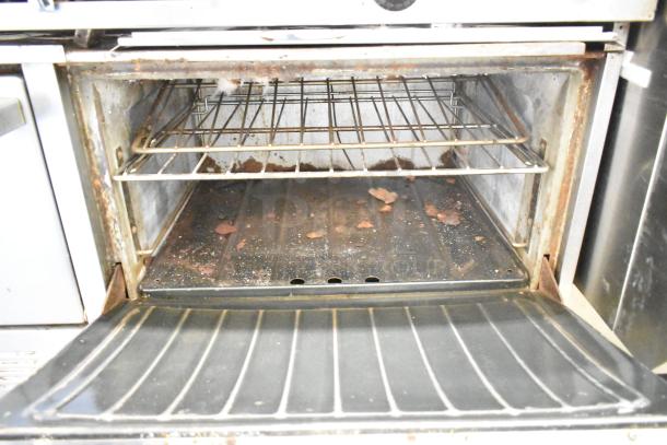 Commercial gas-powered 10-burner range with two ovens, over shelf, and backsplash. Visible wear and residue inside oven.