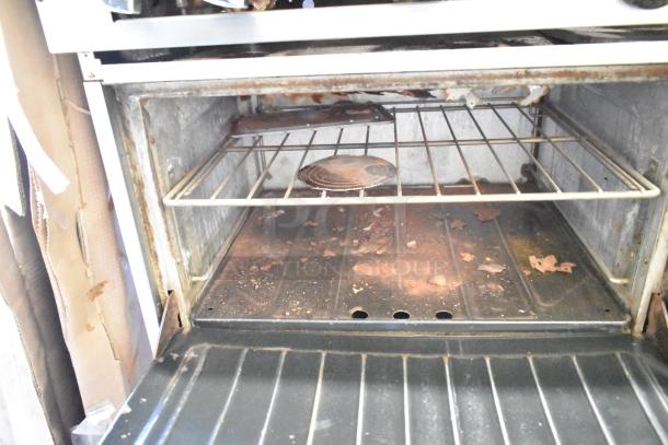 Commercial gas-powered 10 burner range with 2 ovens, over shelf, and backsplash. Visible wear on the oven interior.