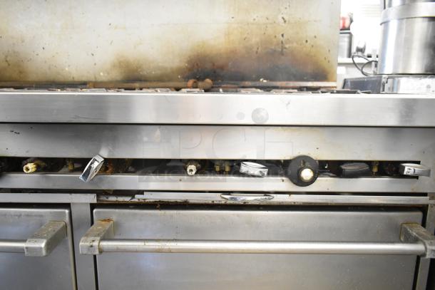 Commercial gas-powered 10 burner range with 2 ovens, overhead shelf, and backsplash. Used condition, visible wear.