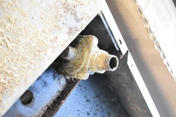 Rusty connection joint on the underside of a commercial gas-powered 10-burner range, indicating wear.
