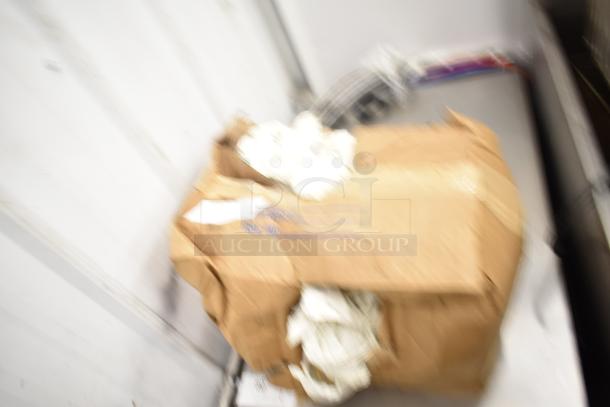 Blurry image of a cardboard box containing various items, including metal pizza pans and lightbulbs. Packing materials visible.