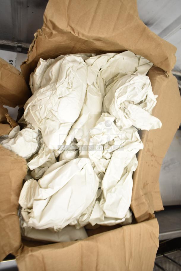 Box with crumpled packing paper possibly containing 9 various items, including metal pizza pans and lightbulbs.