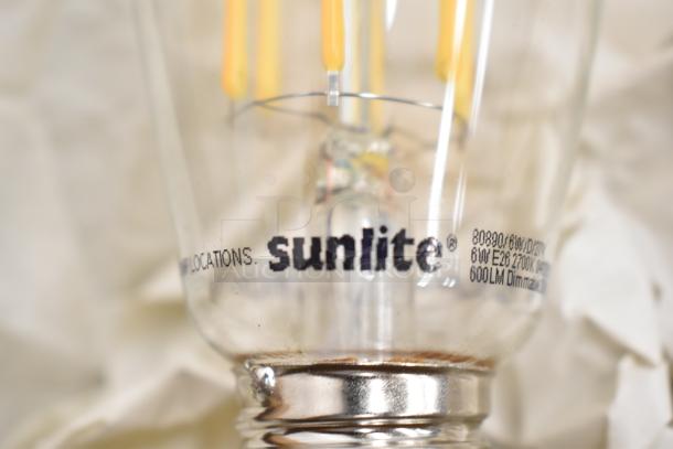 Sunlite 60W E26 2700K dimmable light bulb, 600 lumens, part of a 9-item auction lot including metal pizza pans.