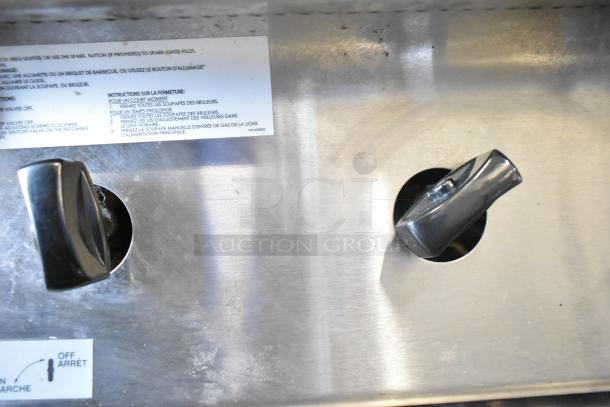 US Range gas-powered 8 burner knobs and control panel. Stainless steel finish, with visible usage wear and instruction label.