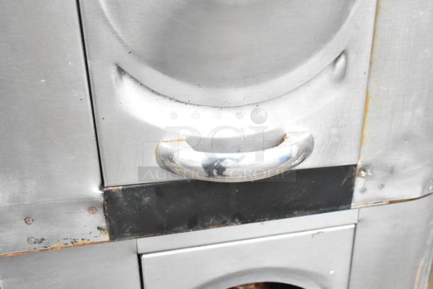 2 Commercial gas-powered single burner pizza ovens with cooking stones, stainless steel, shows wear, sturdy build.