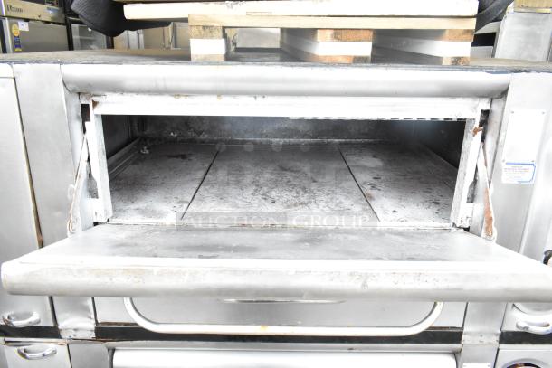 Commercial gas-powered single burner pizza oven with cooking stones, visible wear, stainless steel exterior, open door.