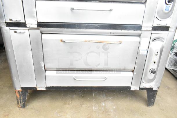 2 Commercial gas-powered single burner pizza ovens with cooking stones, stainless steel, visible wear, sturdy legs.