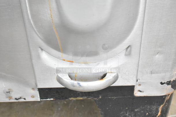 Commercial gas-powered single burner pizza oven detail, featuring a metal handle and surface wear.