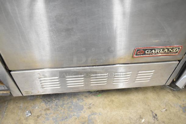 Garland commercial gas 6-burner range with flat top griddle, dual ovens, over shelf, and backsplash; visible Garland logo.
