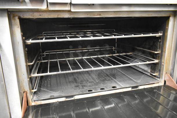 Garland commercial gas range with 6 burners, flat top griddle, dual ovens, shelf and backsplash. Interior view showing oven racks.