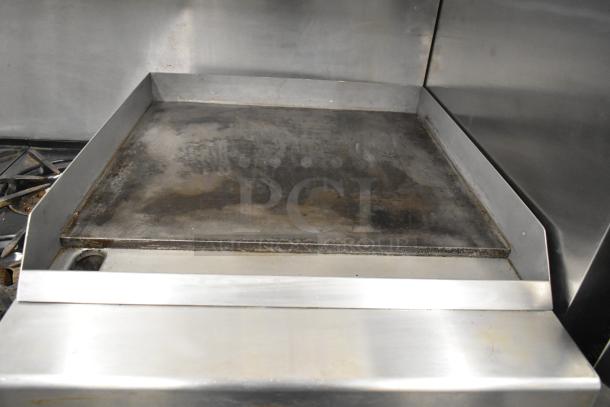Garland commercial gas range with 6 burners, flat top griddle, 2 ovens, over shelf, and backsplash. Used condition.