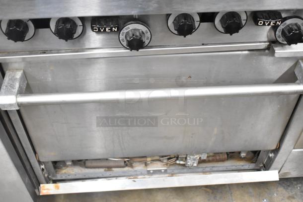 Garland commercial gas range with 6 burners, flat top griddle, 2 ovens, over shelf, and backsplash. Well-used condition.