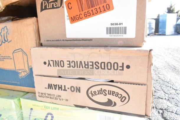 Cardboard boxes labeled "Ocean Spray" and "Purell" stacked, showing packaging for various brand new items. Tags include a barcode and "MGC 6513110.”
