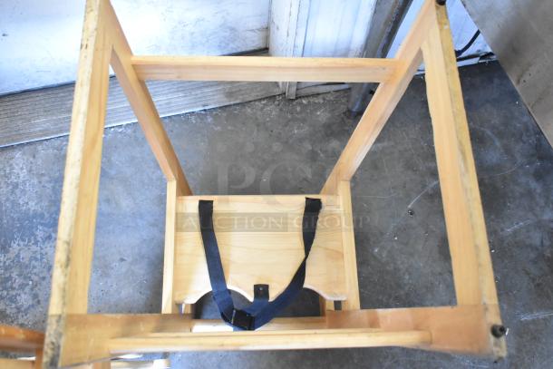 Wooden high chair with harness, light wood finish, sturdy design. Visible wear. Perfect for child seating.