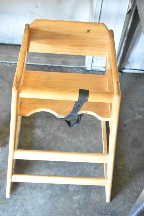 Wooden high chair with safety strap, showing wear. Natural wood finish, sturdy legs. Ideal for toddlers.