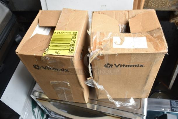 Two VitaMix branded cardboard boxes, slightly worn, potentially containing blender pitchers; labeled with shipping information.