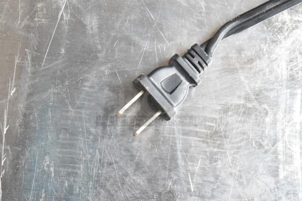 Close-up image of a standard two-prong plug attached to a black cord, resting on a scratched metal surface.