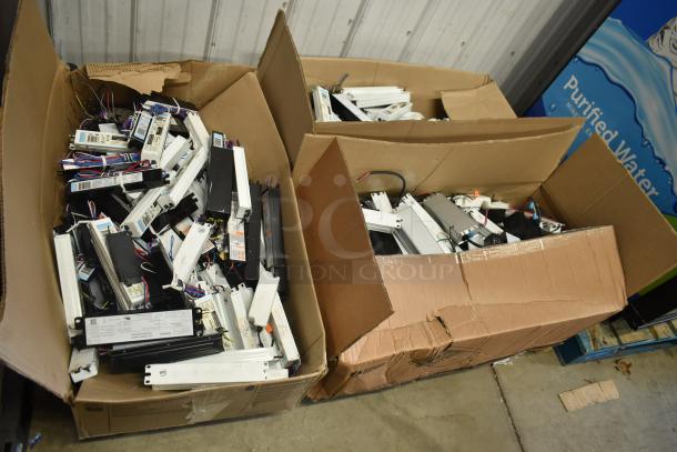 Boxes containing 180 various ballasts for auction. Mix of black and white units, some with visible wiring tags and manufacturer labels.