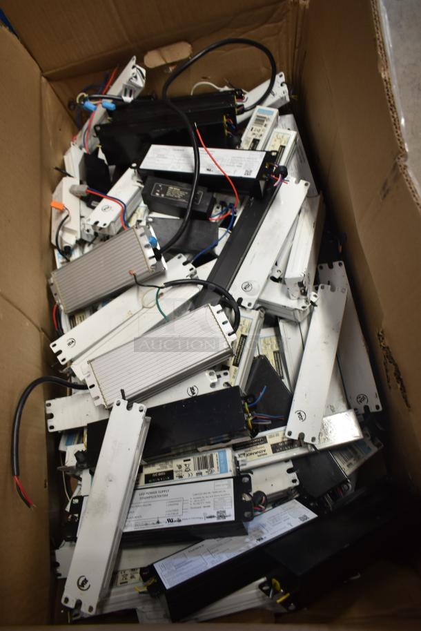 Box of 180 various ballasts, mixed styles and conditions, with visible labels and wiring, ready for auction.