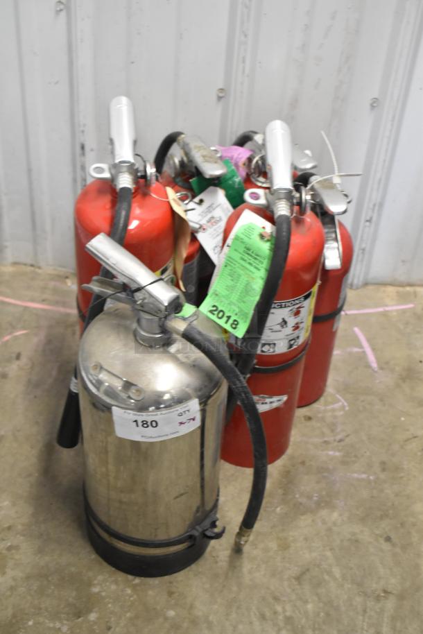 Various fire extinguishers, including red and stainless steel models, with labels and tags indicating condition and 2018 date.