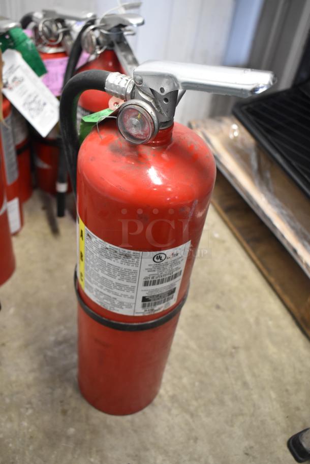 Seven red fire extinguishers with metal handles and gauges, labels indicate multi-purpose use; in good condition. Buyer pick-up only.
