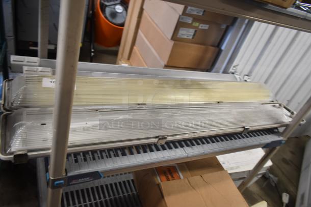 Four industrial light fixtures with clear ribbed covers. Stacked on a metal shelf. Auction label "125" visible.