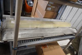 Four industrial light fixtures with clear ribbed covers. Stacked on a metal shelf. Auction label "125" visible.