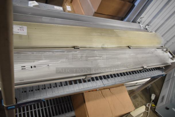 Four industrial light fixtures, ribbed covers, QTY x4 tag visible, used condition, ideal for commercial spaces.