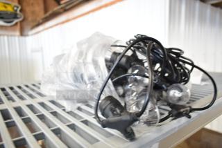 String of lights with clear bulbs and black cords, wrapped in plastic. Appears in good condition on a metal shelf.