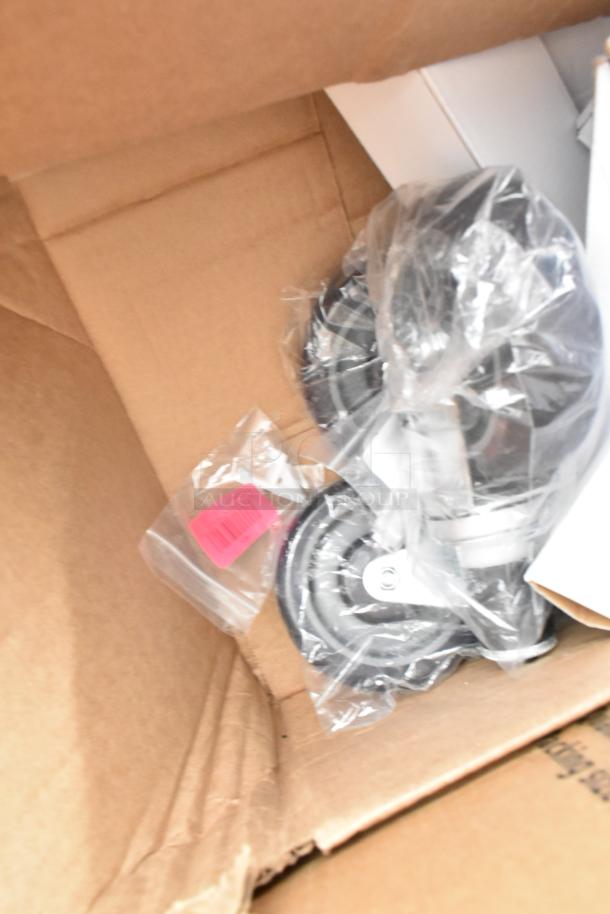 Cardboard box containing new, packaged items including table base pieces and a waitress stand. Visible barcode label.