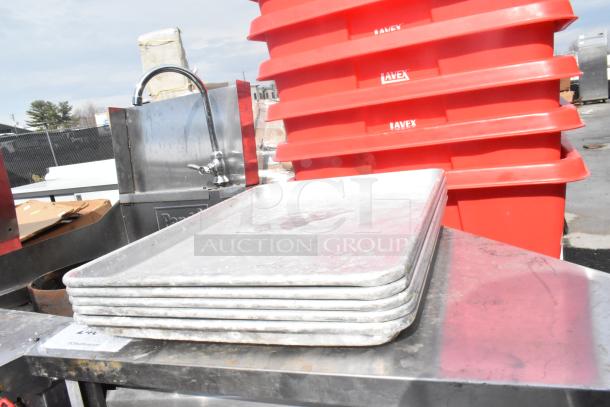 Stack of 5 metal half-size baking pans, used condition, on a metal surface, with red bins labeled "LAVEX" in background.