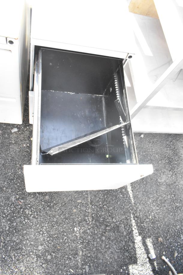 Gray metal 2-drawer filing cabinet with one open drawer, showing interior. Slightly worn. Auction includes two units.