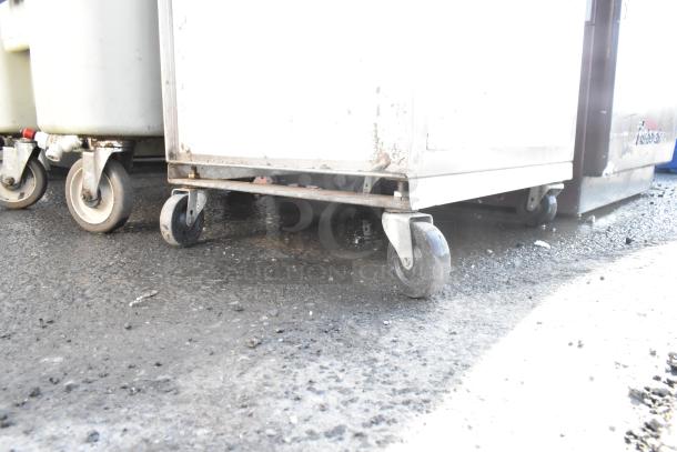 Dish cart on commercial casters, worn condition; sturdy metal frame, four wheels for mobility, ideal for heavy-duty use.