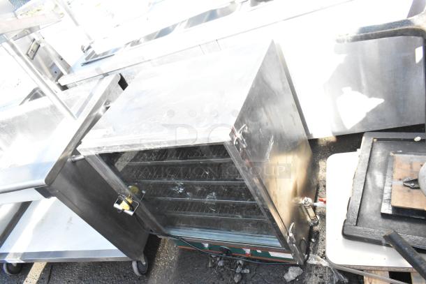 Commercial heated holding cabinet with open double doors, shelves visible, on casters, used condition, stainless steel finish.