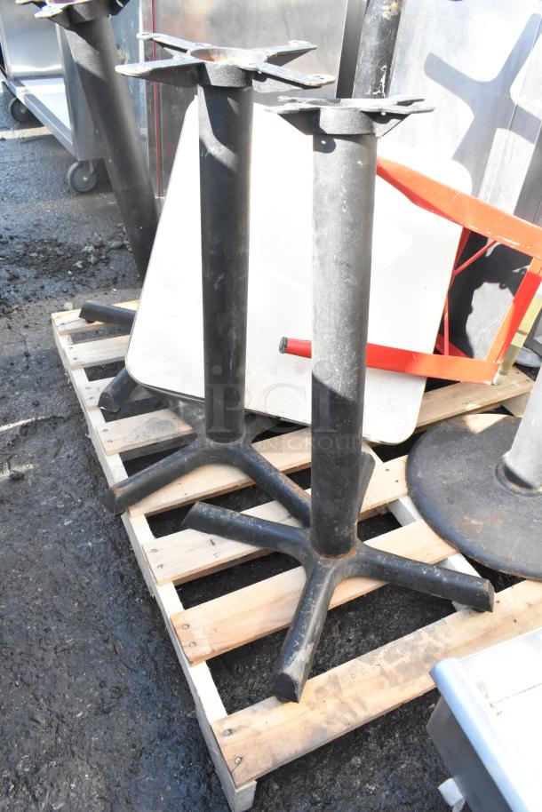 Five black metal table bases on a wooden pallet. Used condition, ideal for commercial or home use.