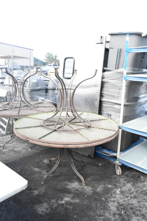 4 mesh patio tables with round tops, weathered metal frames, and lattice design, stacked upside down, suitable for outdoor use.