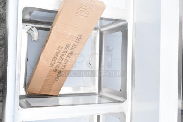 Three-compartment Regency 600S31620218 stainless steel sink with galvanized legs, visible packing box labeled for leg set. Scratch and dent condition.