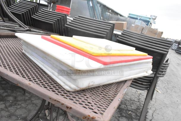 Stack of 10 various cutting boards in white, red, and yellow colors on a metal table, showing moderate use.